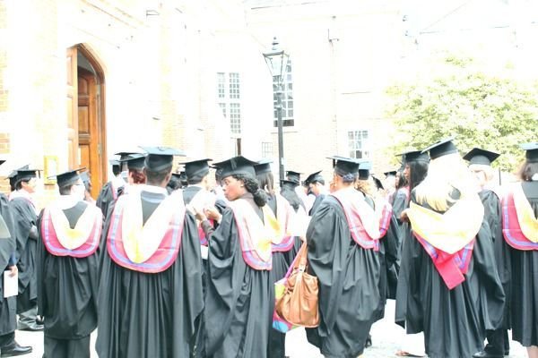 A crowd of IAM graduates in gowns with gold-trimmed hoods outside the hall