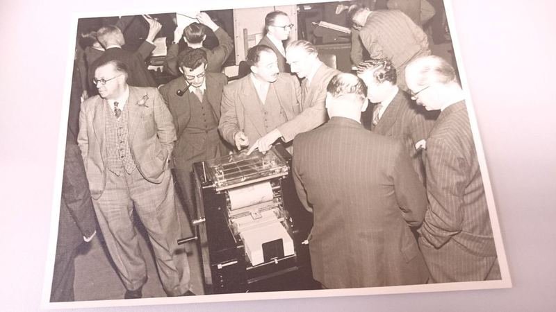 Archive photograph of members in suits examining office machinery at an exhibition